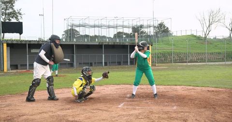 Senior baseball player at pitch with youth batter and local umpire on sports field