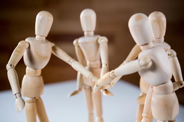 Wooden mannequins hand stacking symbolizes teamwork, unity, and collaboration. Ideal for illustrating concepts of support, partnership, and group efforts in business presentations, educational materials, and motivational content.