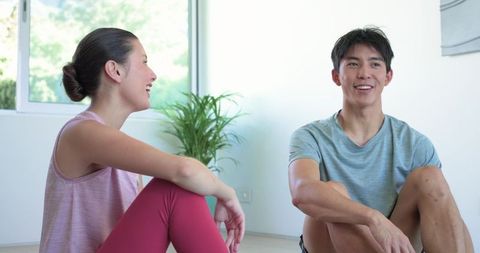 Workout partners sitting on floor after home workout smiling and relaxing in bright room