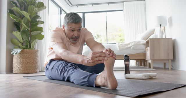 Middle-aged man stretching on yoga mat in living room at home. Ideal for demonstrating morning routines, home fitness exercises, or promoting healthy lifestyles and self-care practices.
