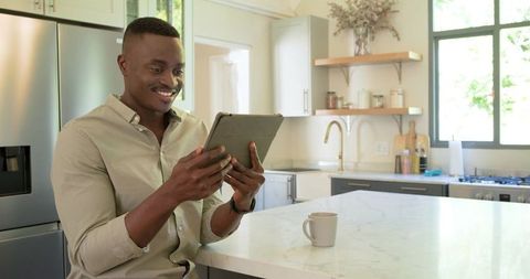 African American Man Smiling While Using Tablet at Modern Marble Kitchen Island