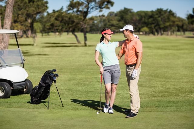 Couple enjoying a sunny day on a golf course, standing next to a golf cart and golf clubs. Ideal for use in advertisements promoting golfing, outdoor activities, sportswear, and leisure activities. Perfect for illustrating themes of bonding, recreation, and healthy lifestyle.