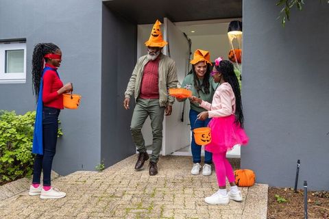 African american family welcoming kids in halloween costumes at front door