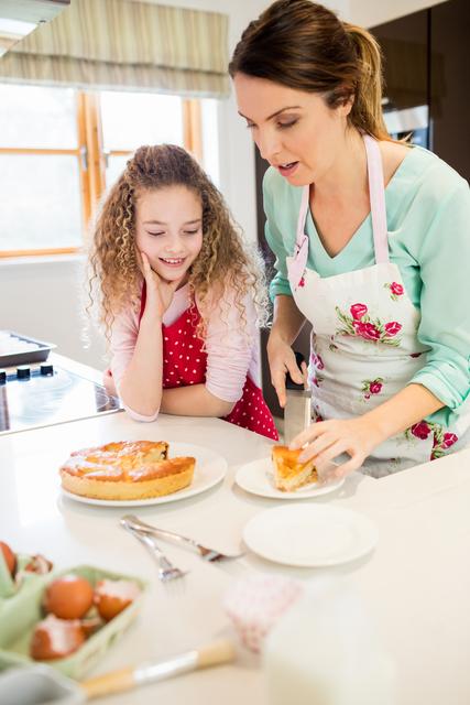 This image captures a mother and her daughter in a warm, home kitchen. The mother is slicing a pancake while the daughter watches with a smile. Perfect for illustrating family bonding, home cooking, parenting, and domestic scenes. Ideal for use in articles, advertisements, or blogs about family activities, recipes, cooking tips, and parenting advice.