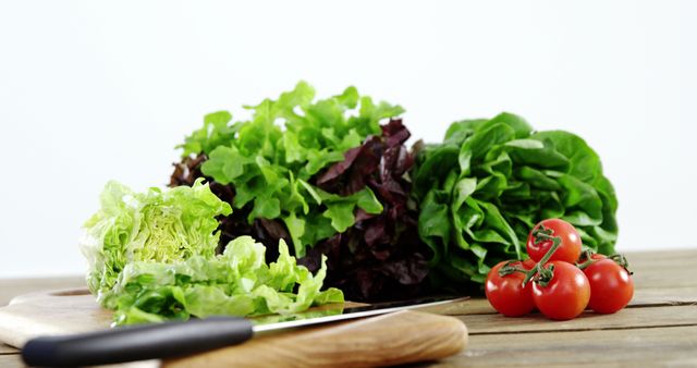 Fresh green lettuce and ripe red tomatoes are arranged on a wooden table, with copy space. These ingredients are commonly used in salads and represent a healthy, vegetarian food choice.