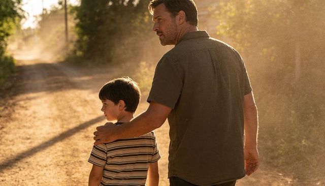 Father guiding son along dusty country road at golden hour warm backlit family bond