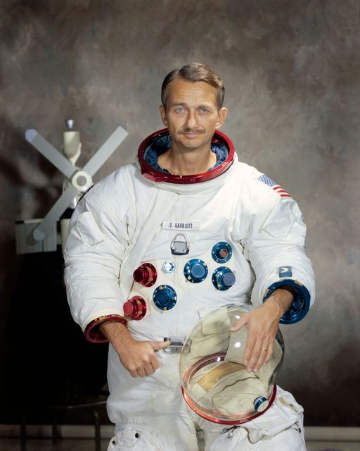 Owen K. Garriott, a distinguished astronaut, stands proudly in his spacesuit holding his helmet, against a plain backdrop. This image, dated September 21, 1971, highlights the era of space exploration and astronaut representation by NASA. Ideal for use in educational materials, history content, and articles on space missions and astronauts.