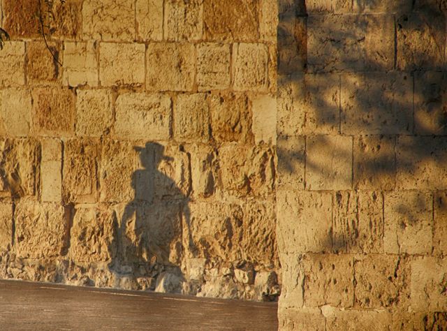 Shadow of a person cast on a historic stone wall illuminated by sunlight. Ideal for travel blogs, historical sites, tourism promotion, or articles on architecture and ancient structures.
