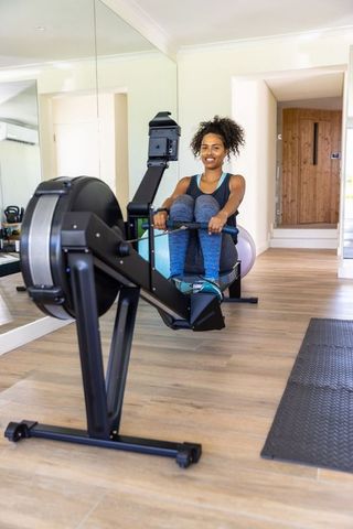 African american woman exercising on rowing machine in home gym