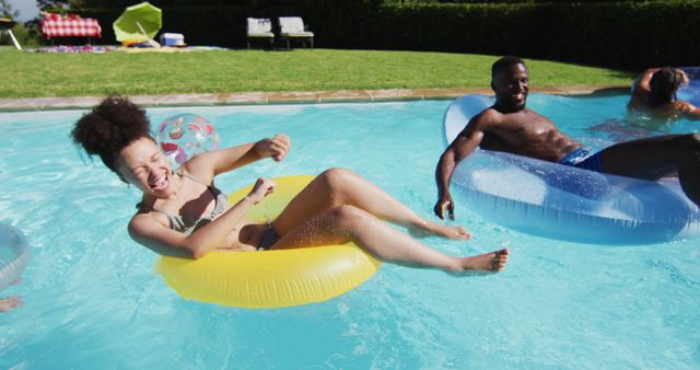 Group of friends enjoying a fun pool party in summer. They are laughing and having a good time while floating on inflatables in the pool. Suitable for promoting summer activities, leisure products, and vacation destinations.