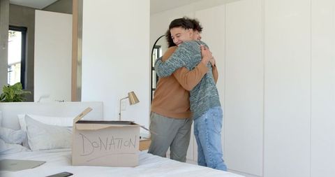 Father and Son Hugging by Donation Box in Cozy Bedroom