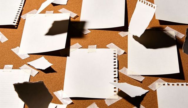 Blank Perforated Notepad Sheets Taped to Cork Board with Torn Paper and Strong Shadows
