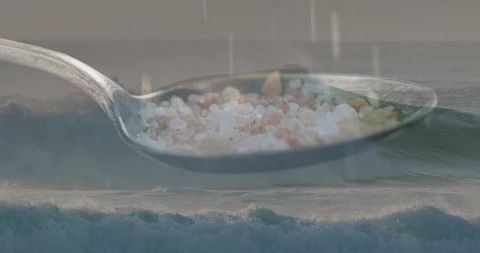 Floating spoon carrying pink Himalayan salt crystals over stormy ocean waves surreal