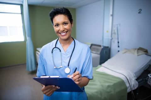 Confident Nurse Standing in Hospital Room with Clipboard