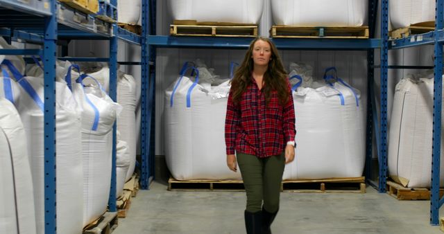 Confident warehouse worker walking among large storage bags, showcasing the industrial and logistic environment. Suitable for themes about logistics, storage solutions, industrial facilities, and warehouse management.