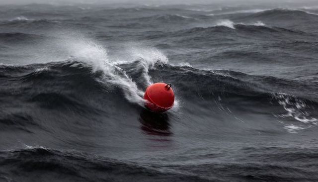 Red buoy bobbing through stormy waves, dramatic minimalist offshore seascape with spray