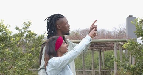 African American man and Indian woman pointing toward pergola in suburban backyard garden