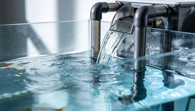 Pouring water from stainless steel spillway into clear glass aquarium display