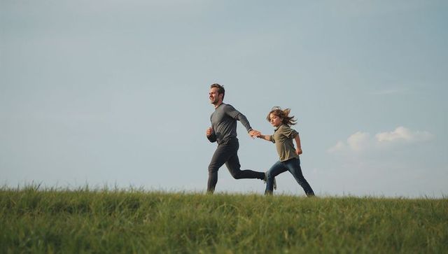 Father and son running hand in hand on grassy ridge for active family bonding