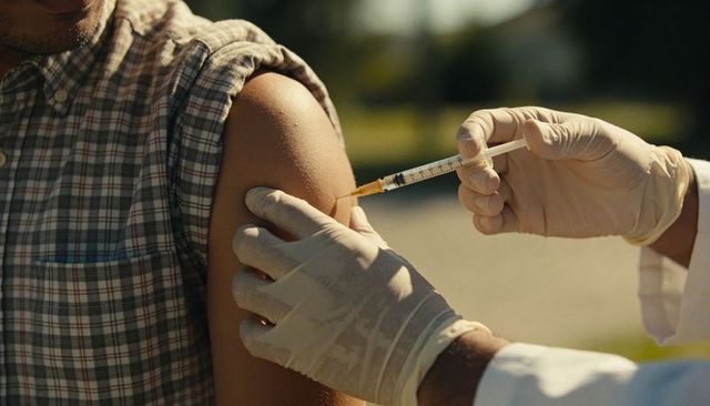 Healthcare worker administering vaccine to patient arm outdoors during sunny clinic