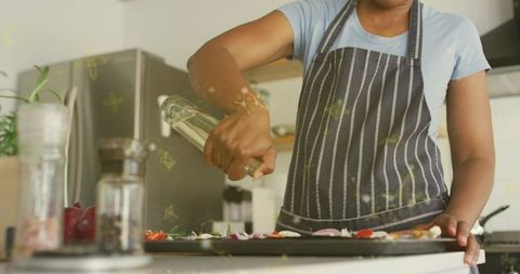 Pouring olive oil over tray of colorful vegetables while preparing healthy home dinner