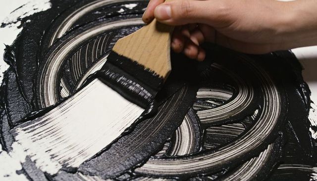 Spreading glossy black paint with flat wooden brush creating monochrome swirls on canvas