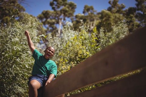Joyful child sitting on wooden railing in sunny park