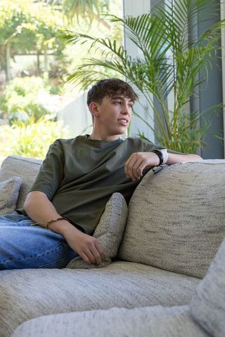Teen leaning back on sofa wearing smartwatch and beaded bracelet in bright living room