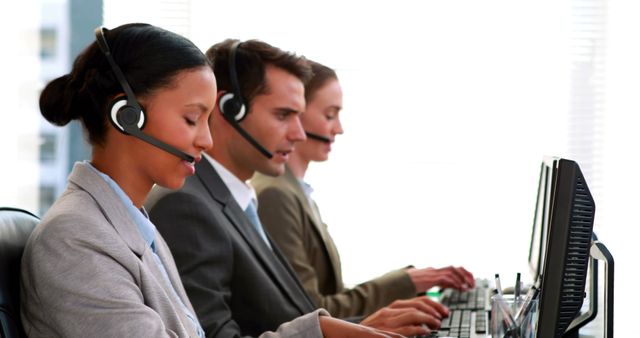 A diverse group of young professionals, customer service representatives, are focused on their computer screens, with copy space. They are equipped with headsets, suggesting they are engaged in handling calls or providing support in a call center environment.