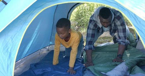 Father and son pitching tent together in park preparing sleeping pads and bags
