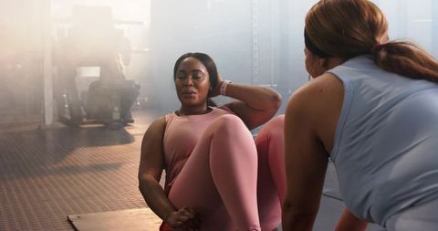 Diverse women performing core workout with trainer on gym floor, teamwork and focus