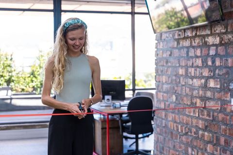 Smiling woman cutting red ribbon at modern coworking space opening ceremony