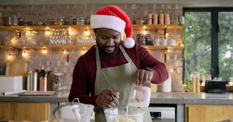 Man baking holiday treats wearing santa hat in cozy kitchen