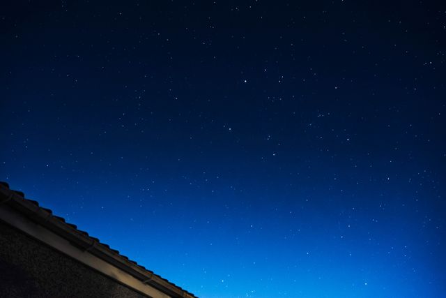 Sky full of stars on a clear night, with a small corner of a roof visible in bottom left. Perfect for themes related to astronomy, tranquility, star gazing, night time contemplation, and outdoor activities.