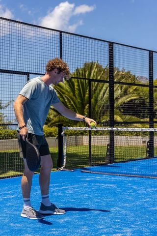 Young man preparing serve on vibrant blue padel court under sunny sky