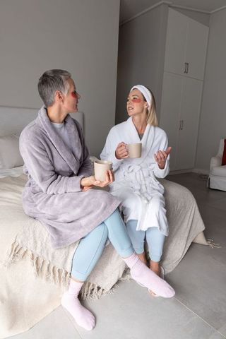 Senior and middle-aged women sharing cozy morning spa rituals in robes with eye patches