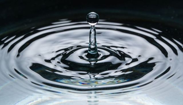Crystal water droplet rising on column with concentric ripples and reflective rings