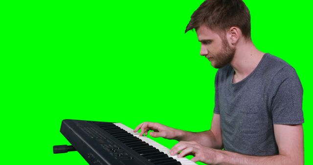 Young man playing electronic keyboard on green screen background, can be used for educational videos on music, online music lessons, promotional content for electronic instruments. Perfect for media requiring music-related visuals with the ability to change background.