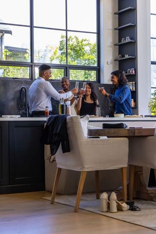 Diverse friends raising glasses and toasting over modern sunlit kitchen island