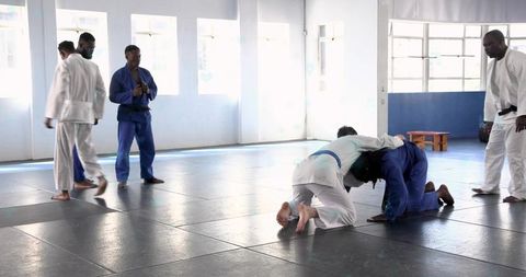 Grappling drill practicing in judo gis on mats inside bright martial arts training hall