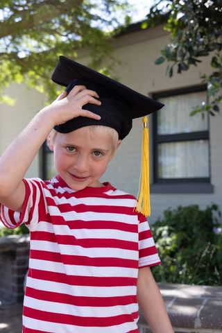 Young boy celebrating graduation wearing mortarboard with yellow tassel and striped tee