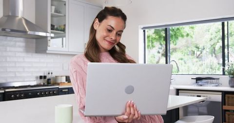 Woman in Pink Sweater Enjoying Laptop in Modern Kitchen