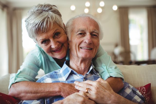 Senior couple sitting on sofa in living room, smiling and embracing. Perfect for use in advertisements, articles, and websites related to senior living, retirement, family, and home life.