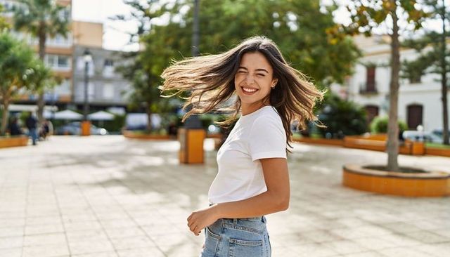 Smiling young woman turning with flowing hair wearing white tee and high-waisted jeans