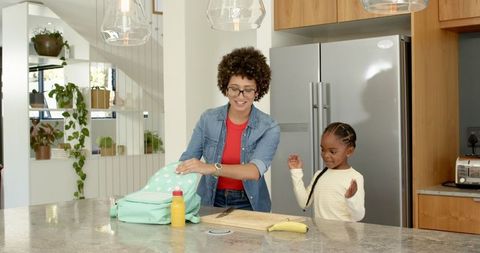 Mother and daughter packing backpack together in kitchen