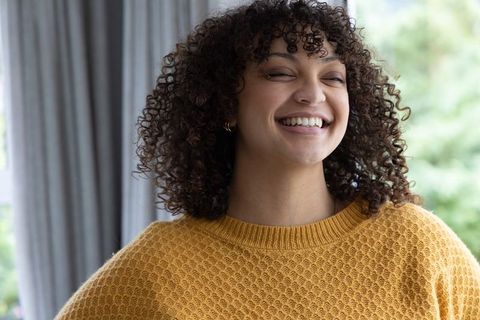 Smiling african american woman wearing mustard knit sweater tilting head by window