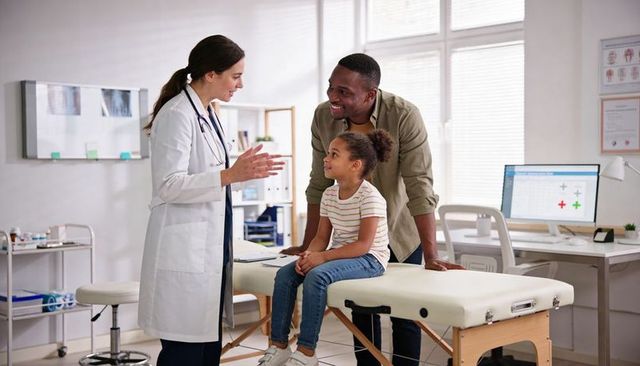 Pediatrician consulting smiling child on exam table with supportive parent in modern clinic