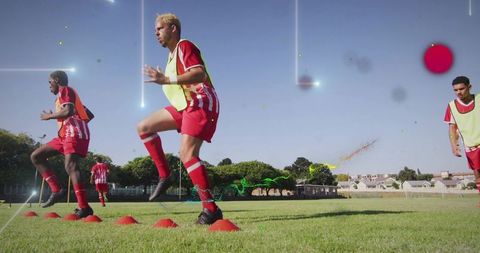 Adult soccer players jumping over cones during team training on grass pitch