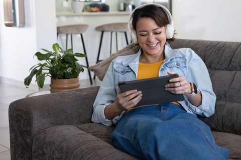 Relaxing african american woman on couch wearing headphones and using tablet at home