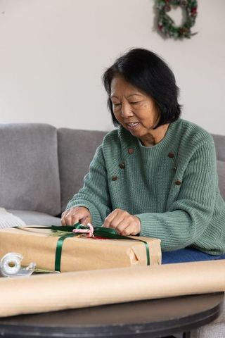 Smiling Senior Woman Wrapping Christmas Gift in Cozy Living Room